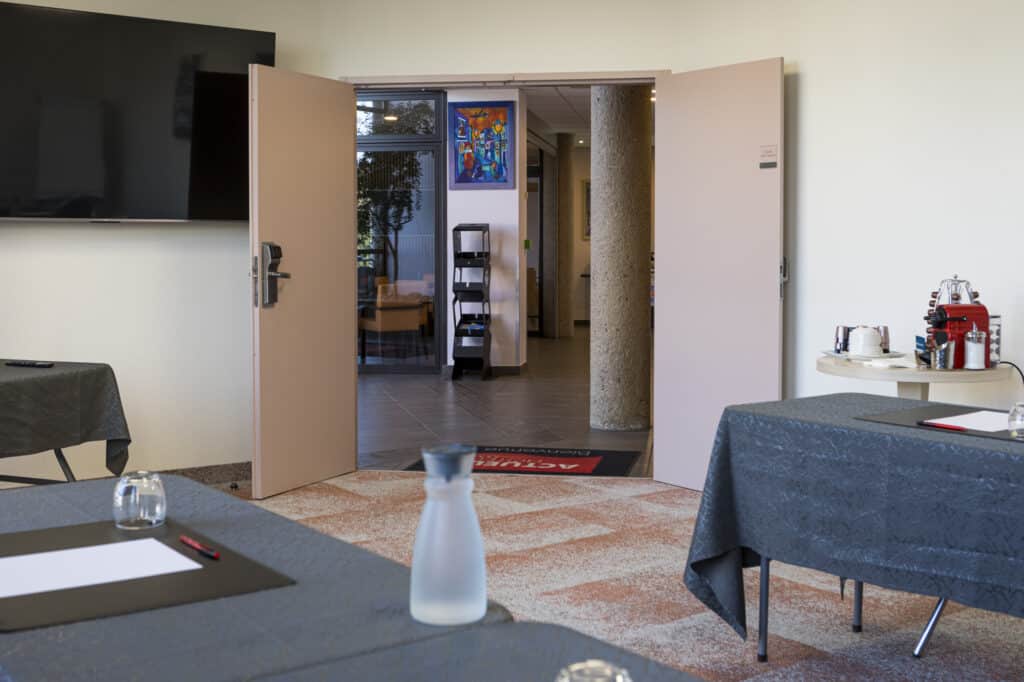 Salle de réunion à l’Actuel Hôtel avec écran de présentation, carafes d’eau et espace café